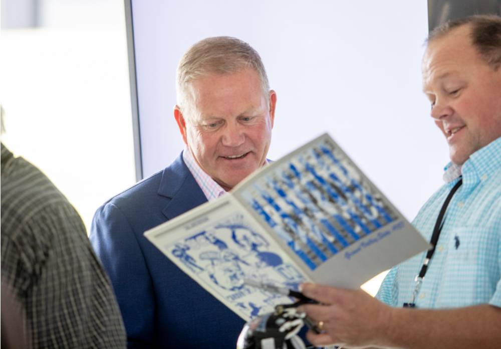 Brian Kelly looking at a book with a guest at the Jamie Hosford Football Center dedication.